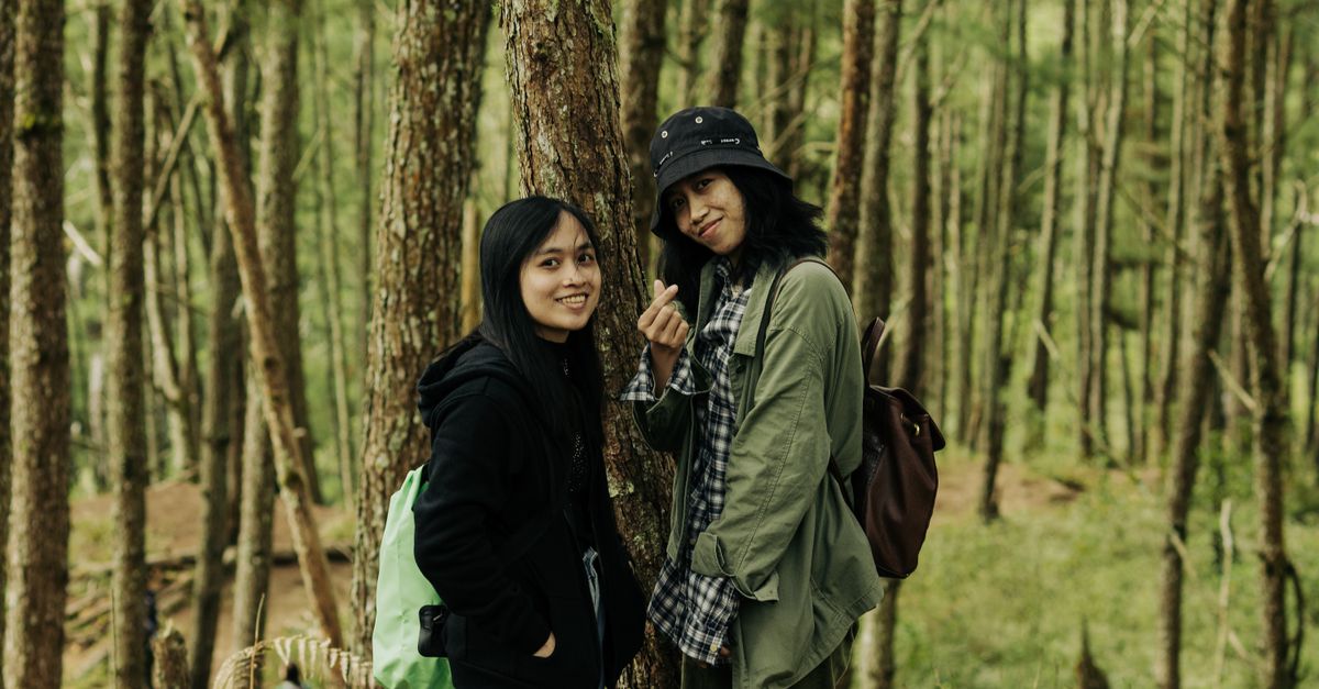 Two women hikers pose in a vibrant forest, embracing nature and friendship.